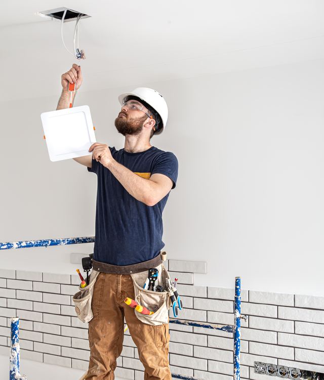 Electricista con casco instalando una luminaria en el techo de una vivienda en obras